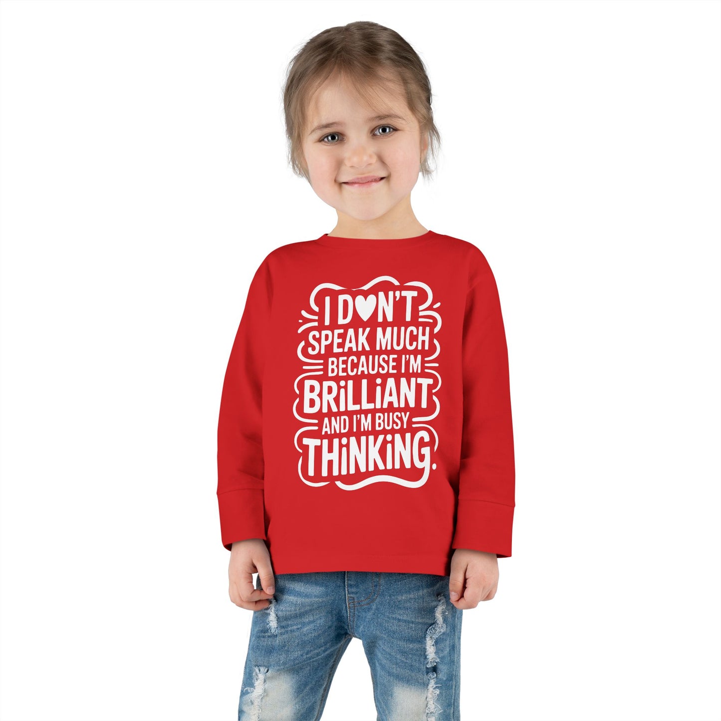 Toddler standing and smiling in red autism acceptance long sleeve tee, showing clear view of the “brilliant and busy thinking” design.
