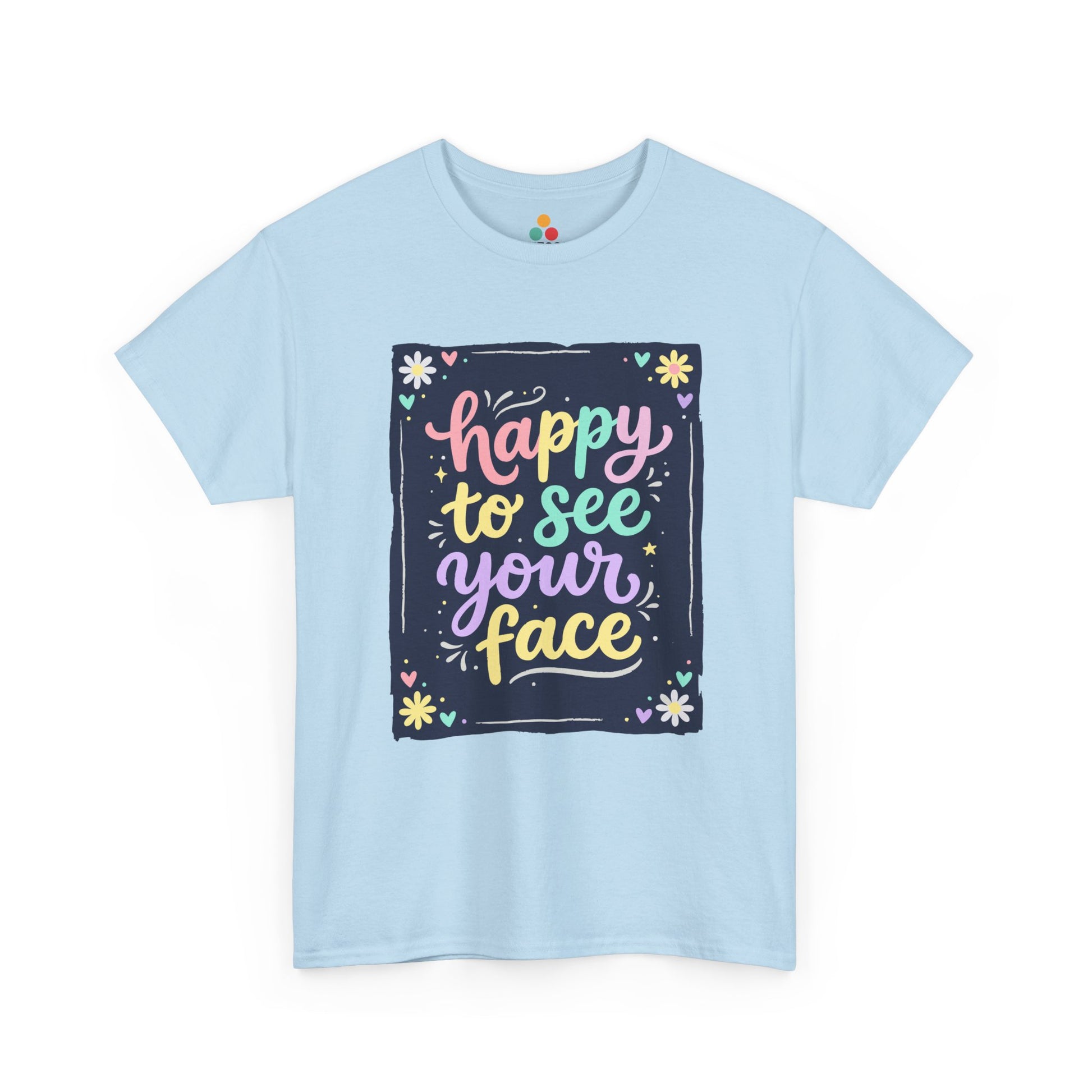 Close-up of a Light Blue T-shirt featuring a colorful "Happy to See Your Face" hand-lettered graphic framed with flowers and hearts on a navy background panel.
