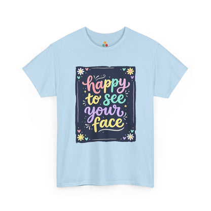 Close-up of a Light Blue T-shirt featuring a colorful "Happy to See Your Face" hand-lettered graphic framed with flowers and hearts on a navy background panel.
