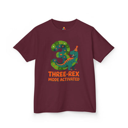 Maroon kids' t‑shirt with colorful green T‑Rex wearing party hat, confetti, and "Three-Rex Mode Activated" text, flat front view.