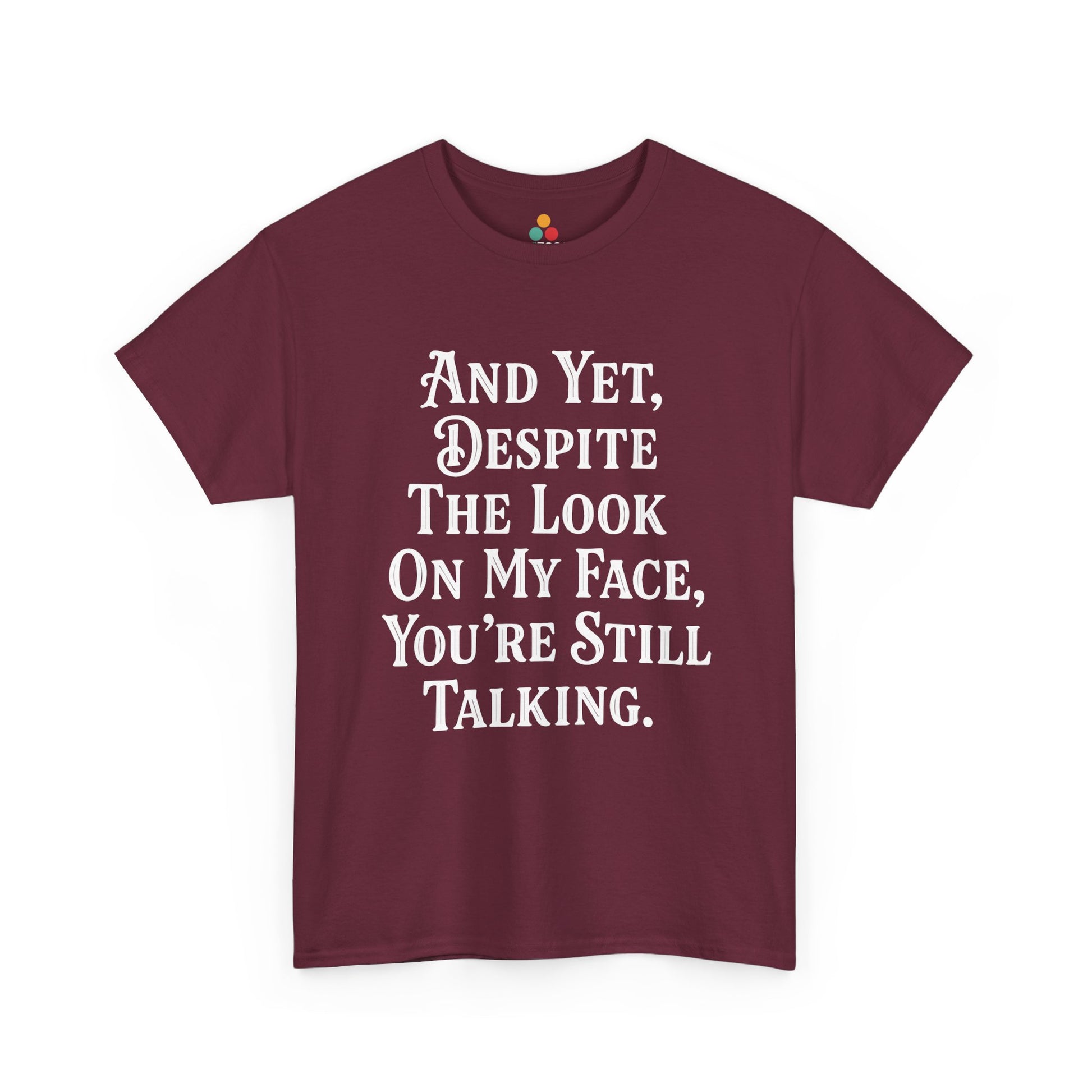 “Teezoca And Yet Despite the Look on My Face You’re Still Talking shirt, funny sarcasm quote in white text, maroon tee, flat front display.”

