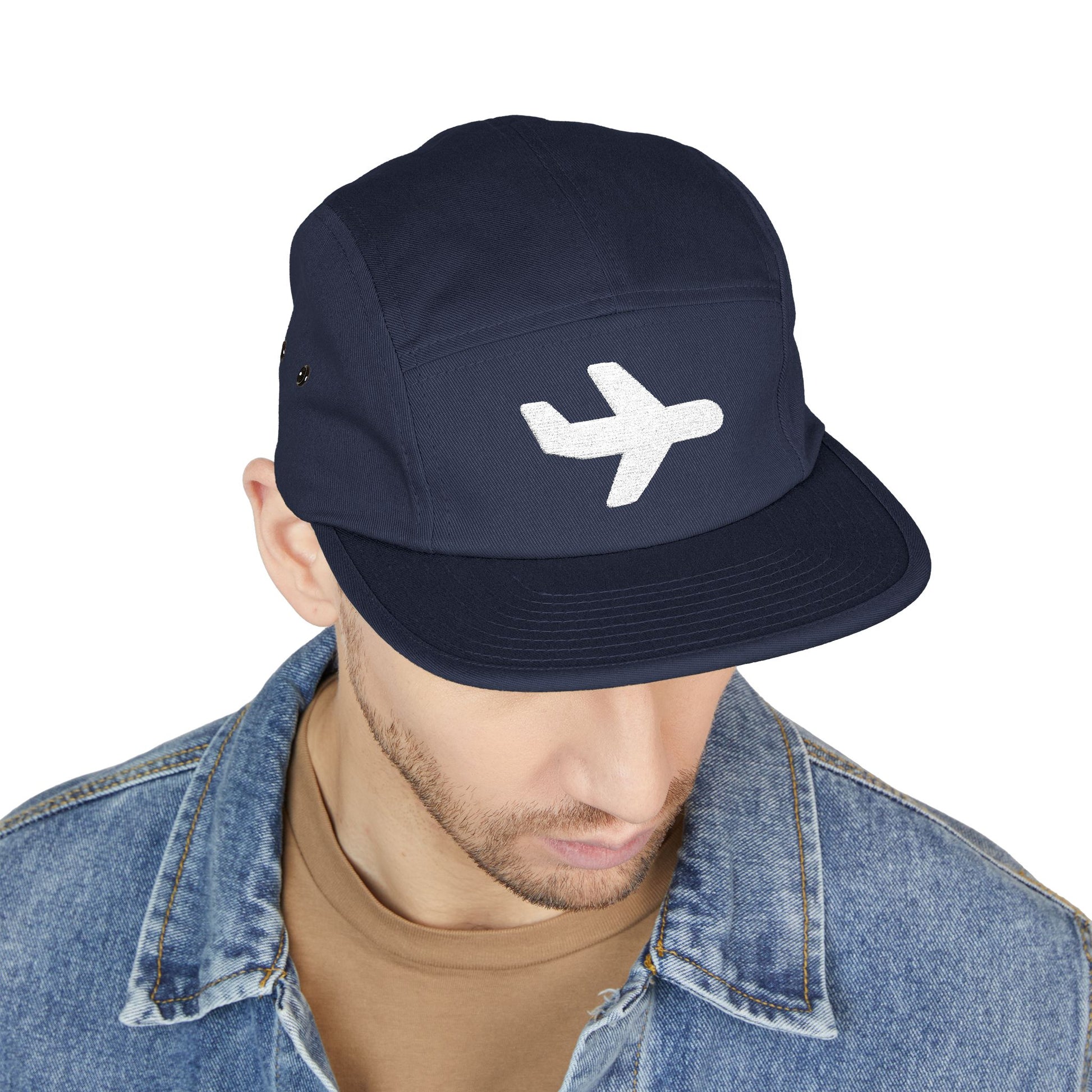 Navy cap with airplane logo worn by a person on a white background. Minimal white airplane icon embroidered on black 5-panel cap. TEEZOCA