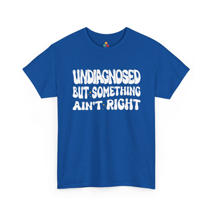 “Teezoca Undiagnosed But Something Ain’t Right t-shirt, bold white bubble text with tiny yellow sparkles, royal blue tee, front.”​

