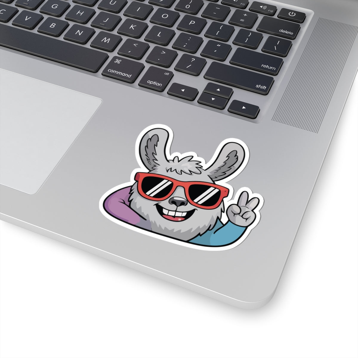 Laptop with a sticker of a cartoon llama wearing sunglasses and giving a peace sign. TEEZOCA