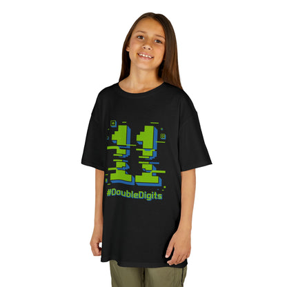 Child wearing a black t-shirt with green and blue graphics and text on a white background  Black kids’ t‑shirt with neon green and blue pixel number 11 and “#DoubleDigits” gamer text, flat front view.