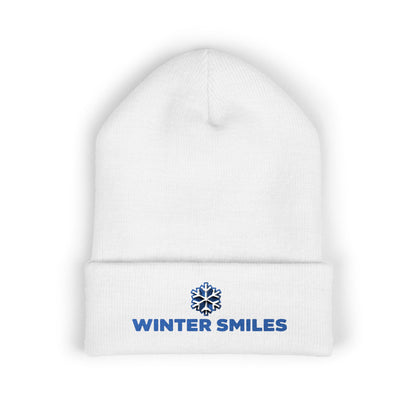 White beanie with 'Winter Smiles' logo on a white background. Blue embroidered “Winter Smiles” snowflake design on cuffed winter beanie