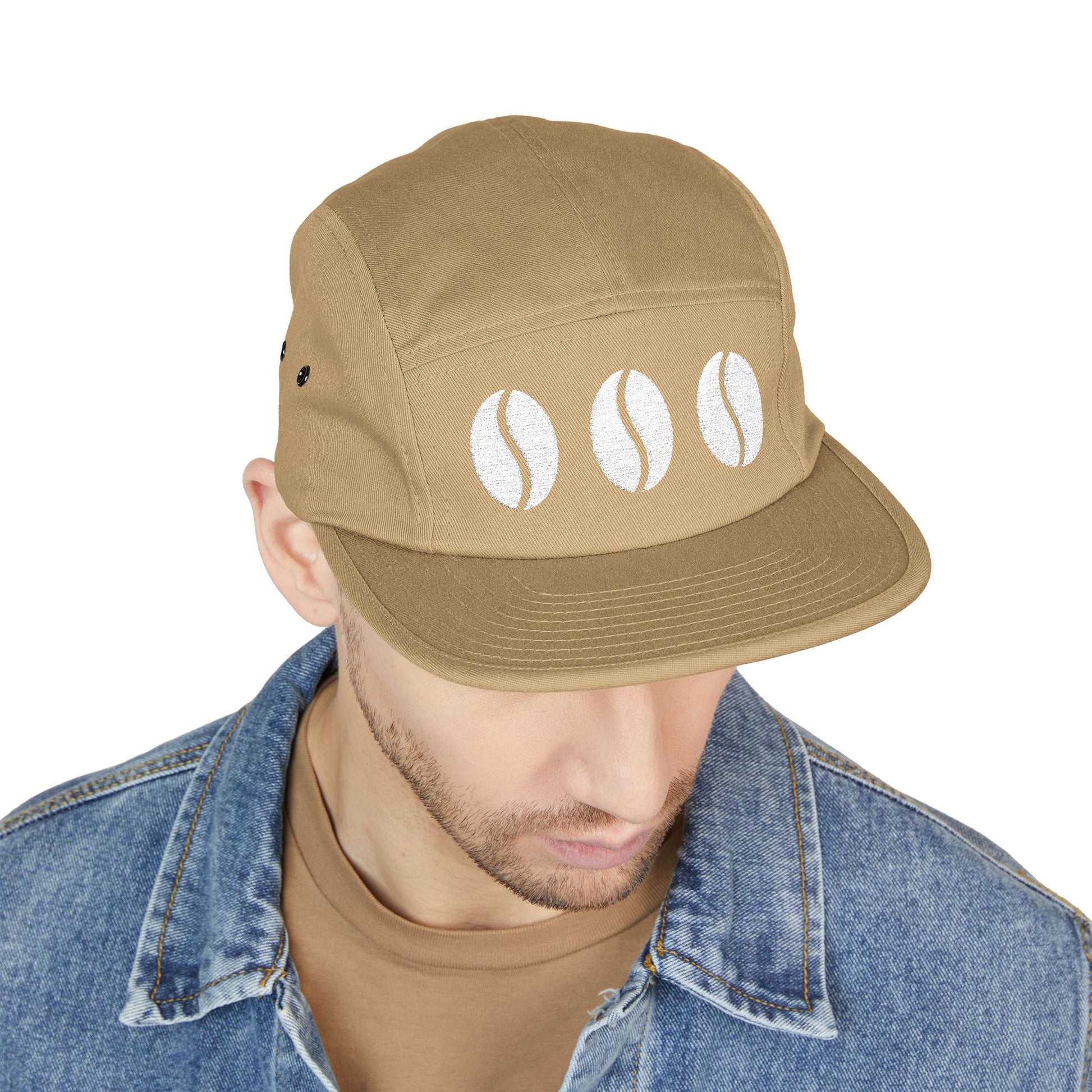 Man wearing a brown cap with coffee bean designs on a white background. Triple coffee bean minimalist embroidery on 5-panel cap. TEEZOCA