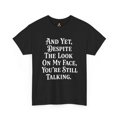 “Teezoca And Yet Despite the Look on My Face You’re Still Talking shirt, bold white serif text, black tee, front view.”

