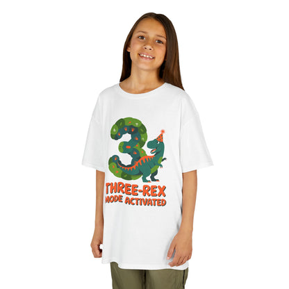 Kids Girl kids' t‑shirt with colorful green T‑Rex wearing party hat, confetti, and "Three-Rex Mode Activated" text, flat front view.