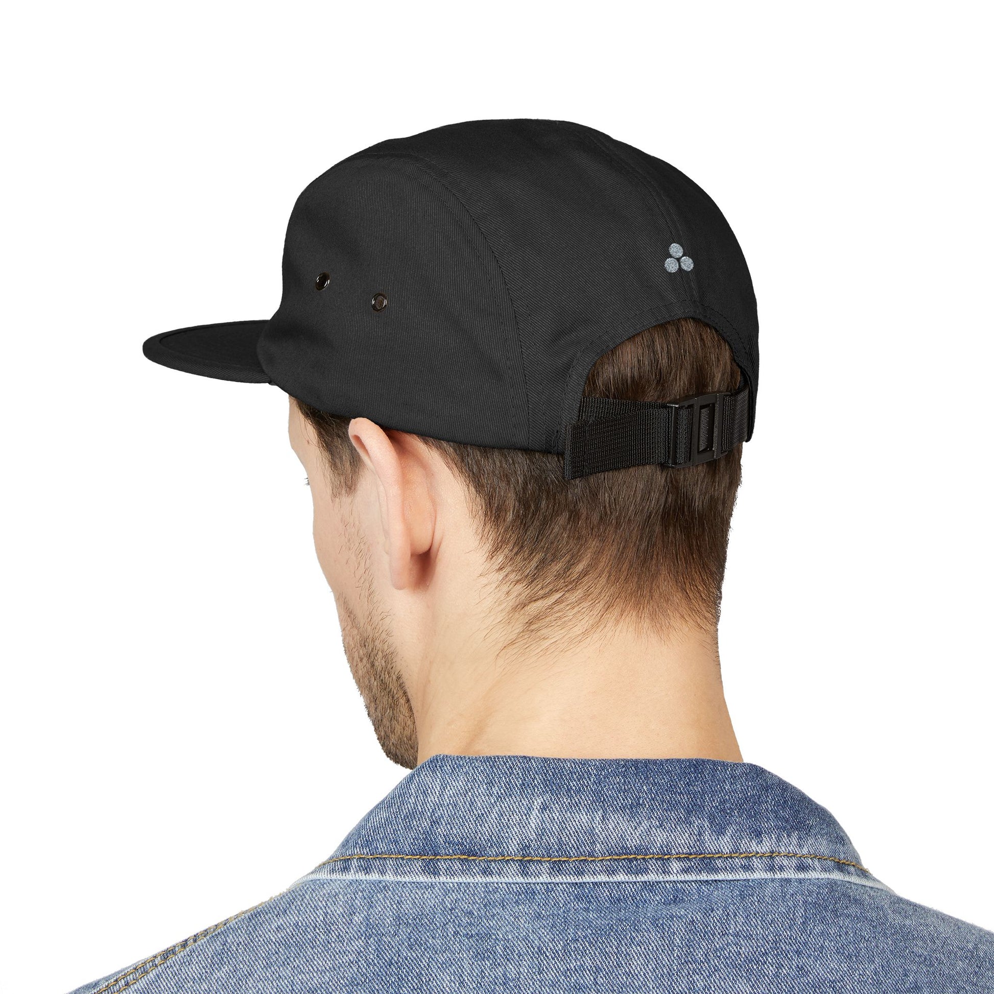Person wearing a black cap with a brand logo on a white background. Minimal embroidered cat icon design on 5-panel cap. TEEZOCA
