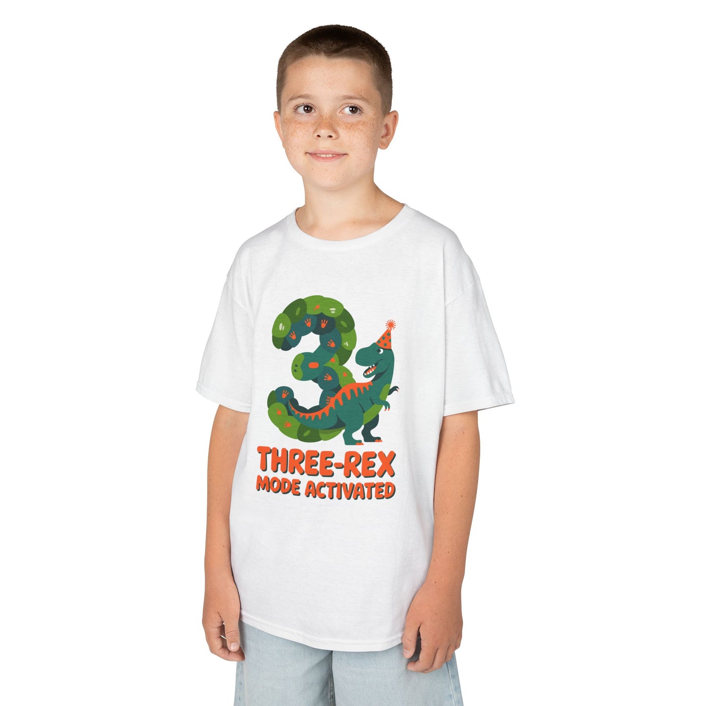  kids' t‑shirt with colorful green T‑Rex wearing party hat, confetti, and "Three-Rex Mode Activated" text, flat front view.