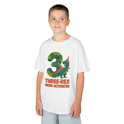  kids' t‑shirt with colorful green T‑Rex wearing party hat, confetti, and "Three-Rex Mode Activated" text, flat front view.