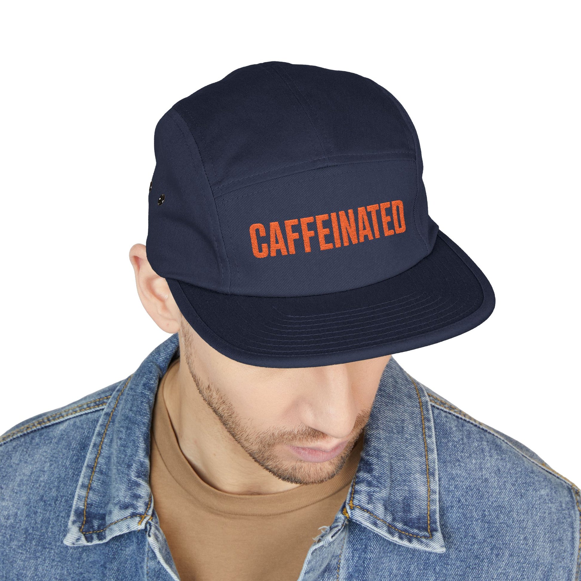 Navy cap with 'CAFFEINATED' text worn by a person on a white background. Minimal text design reading CAFFEINATED in block letters. TEEZOCA