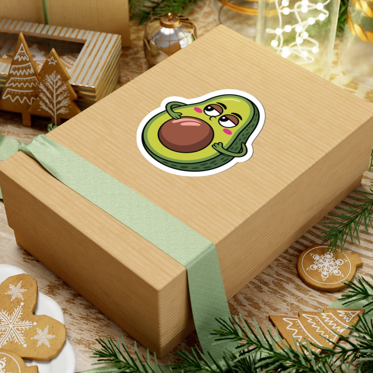 Wooden gift box with a cartoon avocado sticker on a festive background with cookies and lights. TEEZOCA