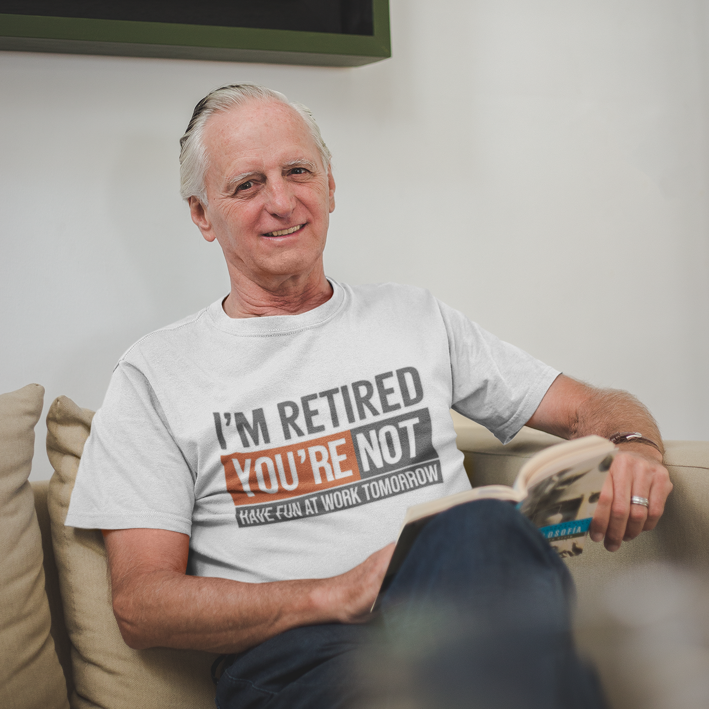 “Older man relaxing on a couch wearing a white Teezoca I’m Retired You’re Not Have Fun at Work Tomorrow shirt, lifestyle mockup, front view.”

