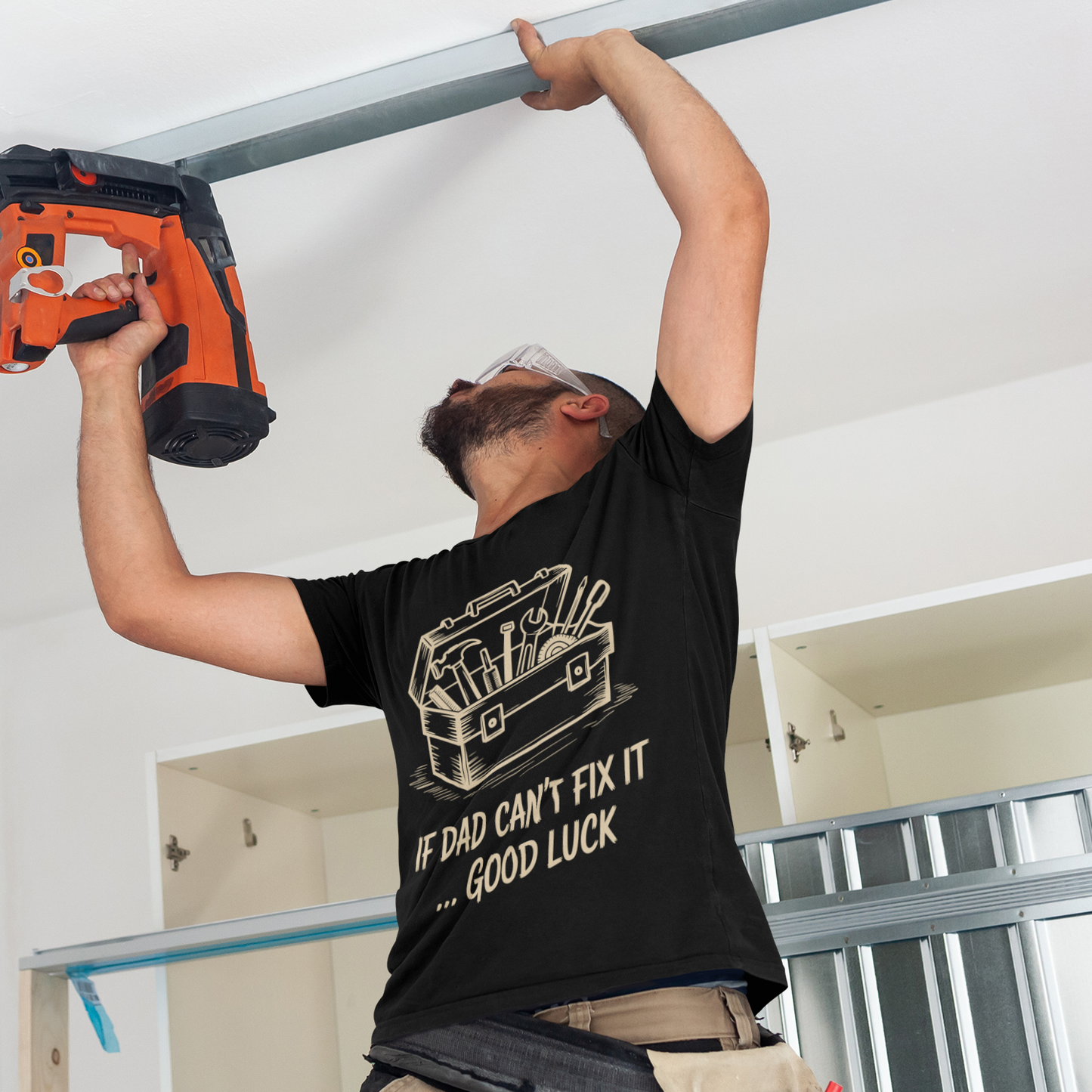 TEEZOCA handyman wearing the “If Dad Can’t Fix It… Good Luck” funny dad T‑shirt while working overhead.