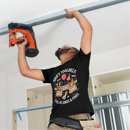 Man wearing a TEEZOCA “Dad’s Toolbelt Full Of Jokes & Fixes” T‑shirt while working overhead with a tool.