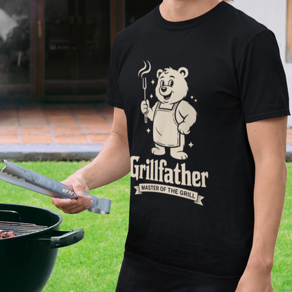 Man wearing a black TEEZOCA “Grillfather Master Of The Grill” funny BBQ dad T‑shirt while standing by a grill.