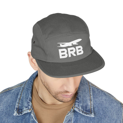Gray cap with 'BRB' and airplane logo worn by a person on a white background. Minimalist BRB airplane embroidered design for 5-panel cap by TEEZOCA
