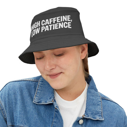 Person wearing a black bucket hat with 'HIGH CAFFEINE, LOW PATIENCE' Funny text on a white background. TEEZOCA
