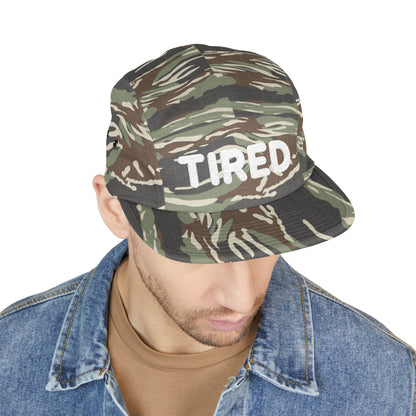 Camouflage bucket hat with 'TIRED' text worn by a person on a white background. TIRED minimalist text embroidered on 5-panel cap by TEEZOCA