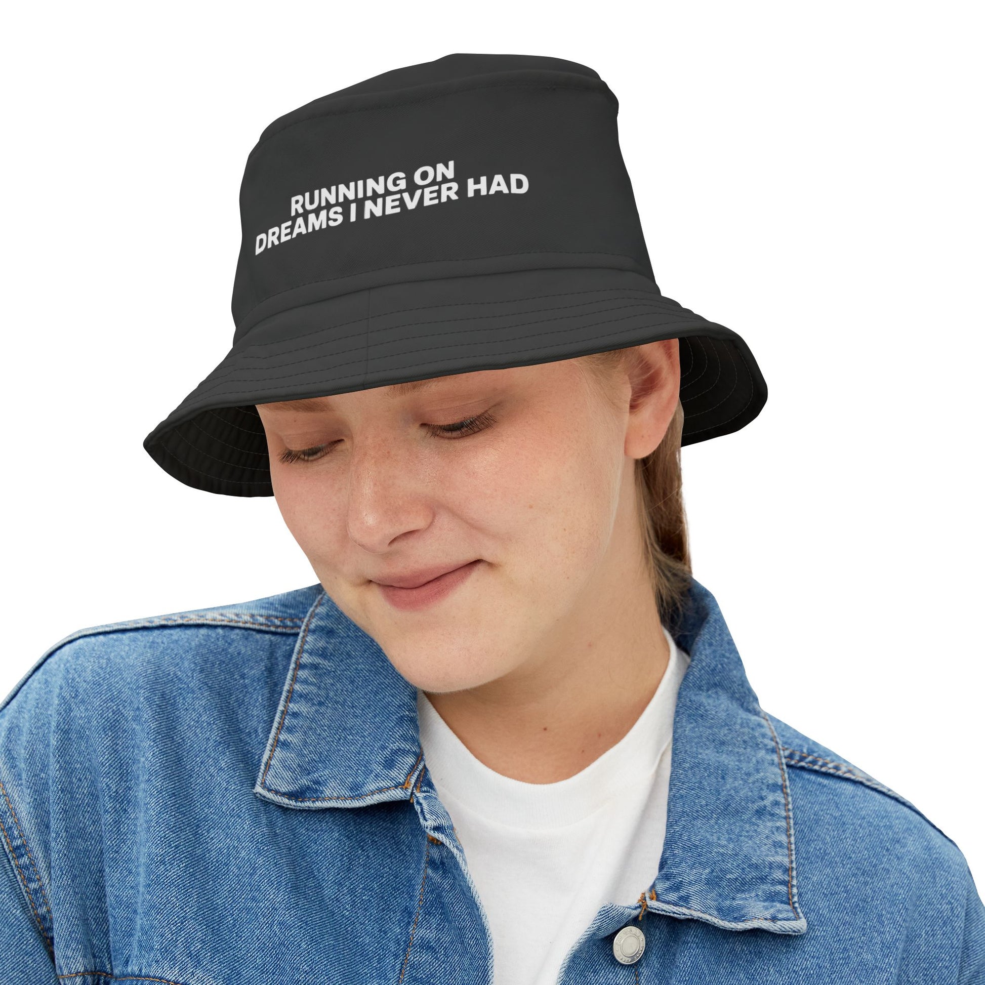 Funny black bucket hat with white text 'RUNNING ON DREAMS I NEVER HAD' on a white background. TEEZOCA