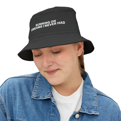 Funny black bucket hat with white text 'RUNNING ON DREAMS I NEVER HAD' on a white background. TEEZOCA