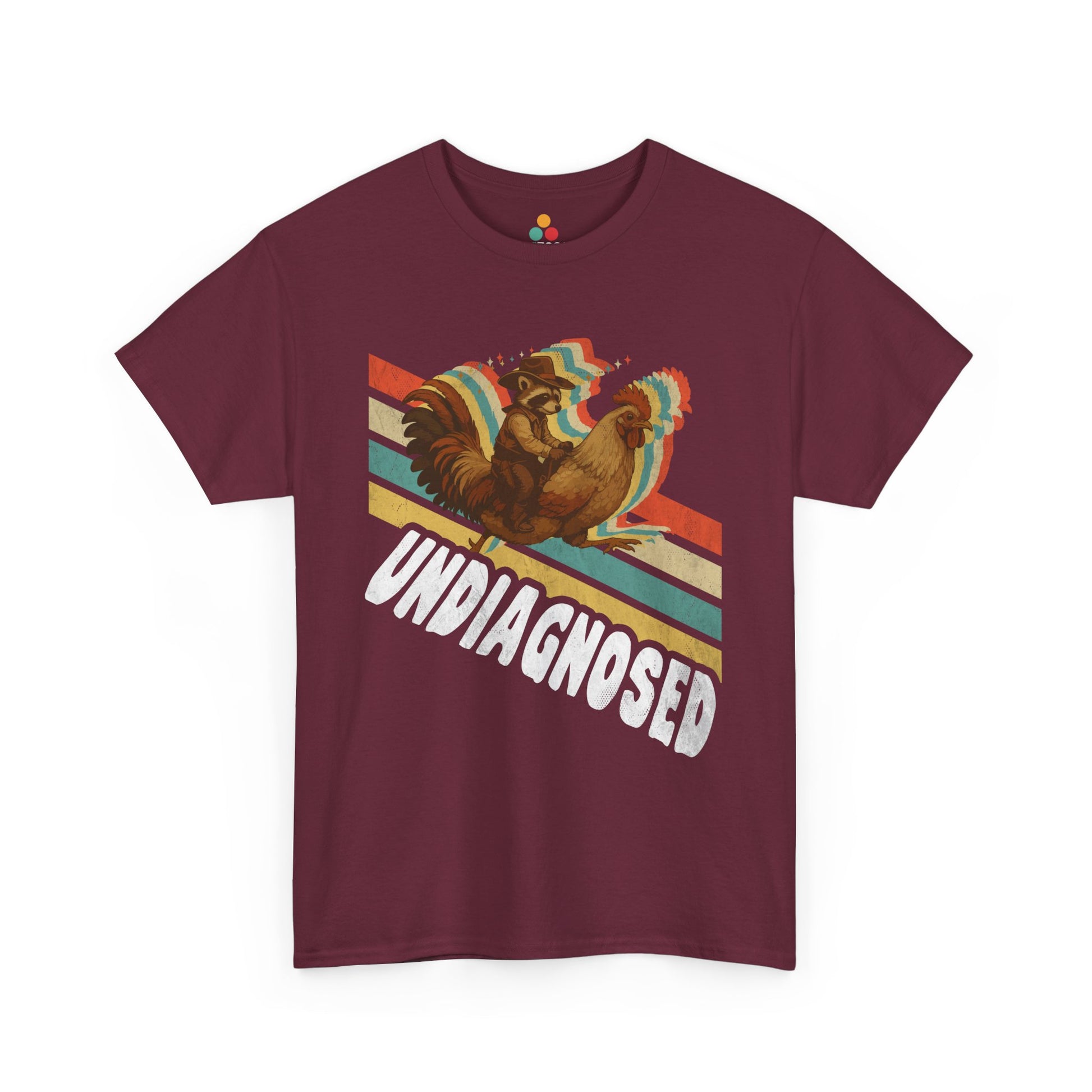 “Teezoca Undiagnosed shirt, cowboy raccoon and rainbow rooster riding graphic, maroon tee, front view.”

