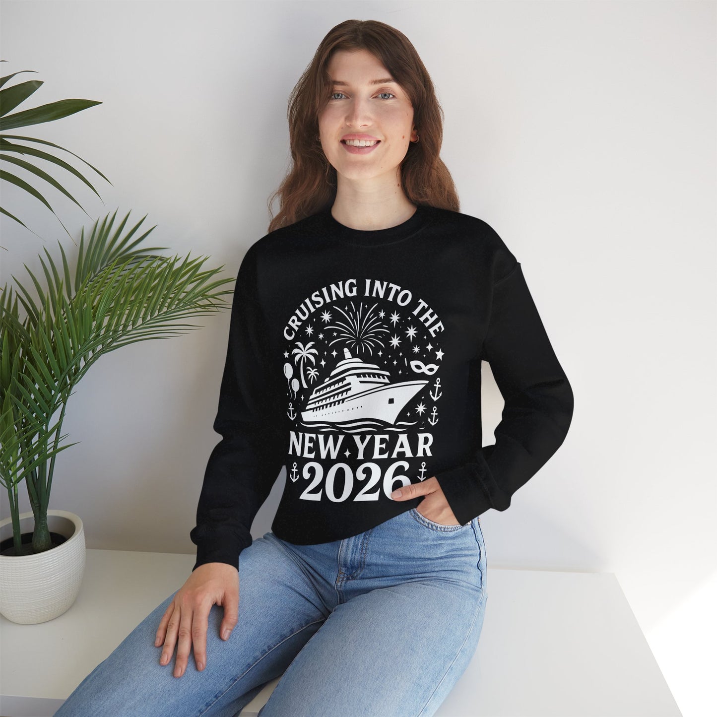 Person wearing a black sweatshirt with New Year's design, sitting on a white surface with a plant in the background.