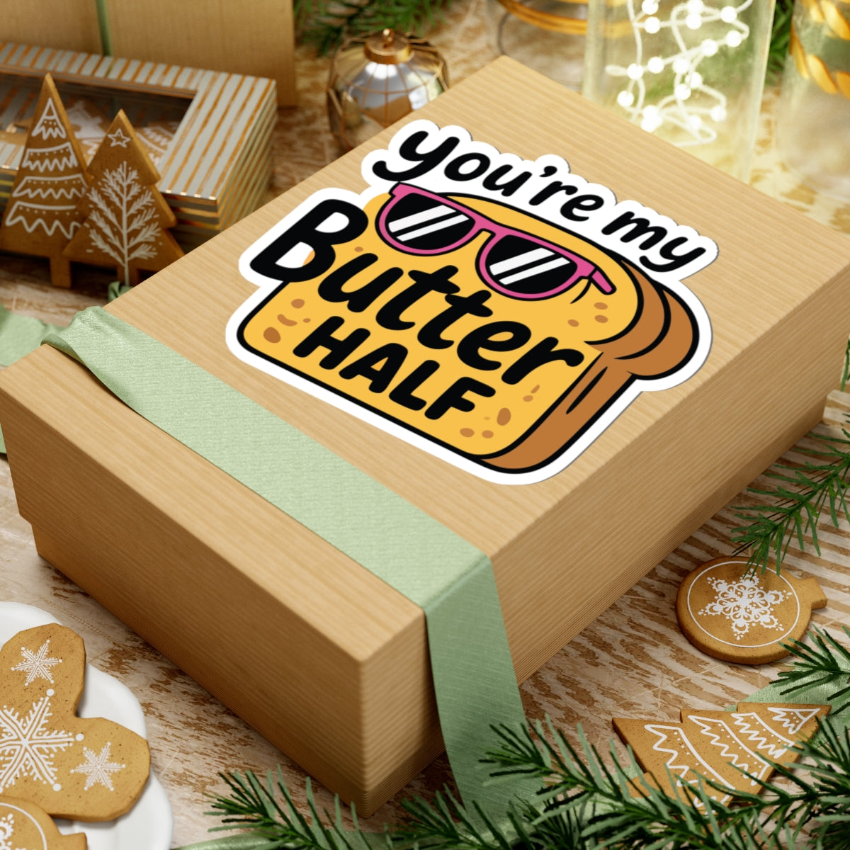 Gift box with 'You're my Butter Half' sticker on a festive background with cookies and lights. TEEZOCA