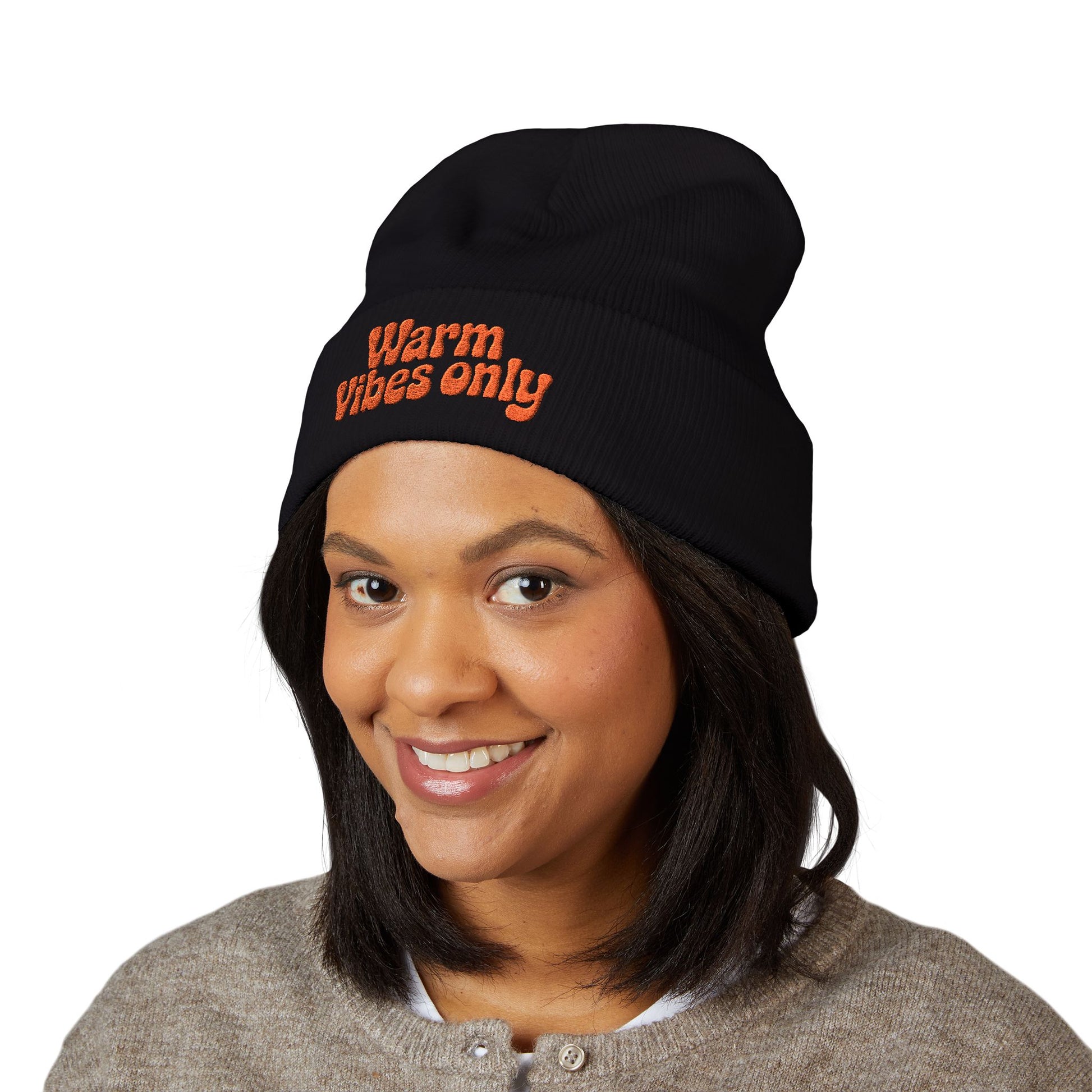 Person wearing a black beanie with 'Warm Vibes only' text on a white background. Black beanie with 'Warm Vibes only' text in orange on a white background. “Warm vibes only” embroidered patch on cozy cuffed beanie in retro orange thread.