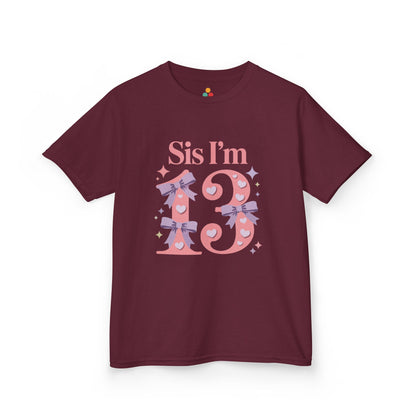 Navy t‑shirt with pink “Sis I’m 13” design featuring hearts, lilac bows, and sparkles, flat front view.