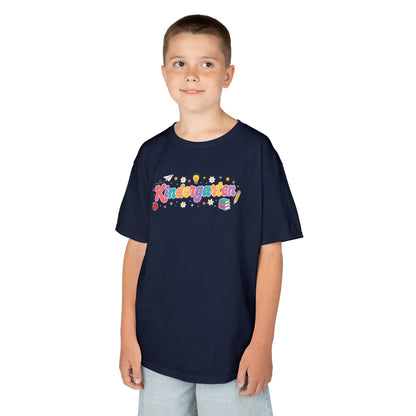 Child wearing a navy blue t-shirt with colorful 'Kindergarten' design on a white background. TEEZOCA t-shirt showing a cute Kindergarten graphic for a back to school kindergarten shirt, with books, pencil, apple, and stars.