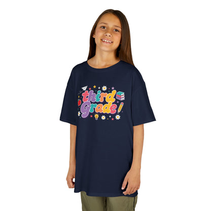Child wearing a navy t-shirt with 'third grade!' printed on it against a white background. TEEZOCA t-shirt with rainbow school lettering for parents browsing a 3rd Grade Shirt for Girls.