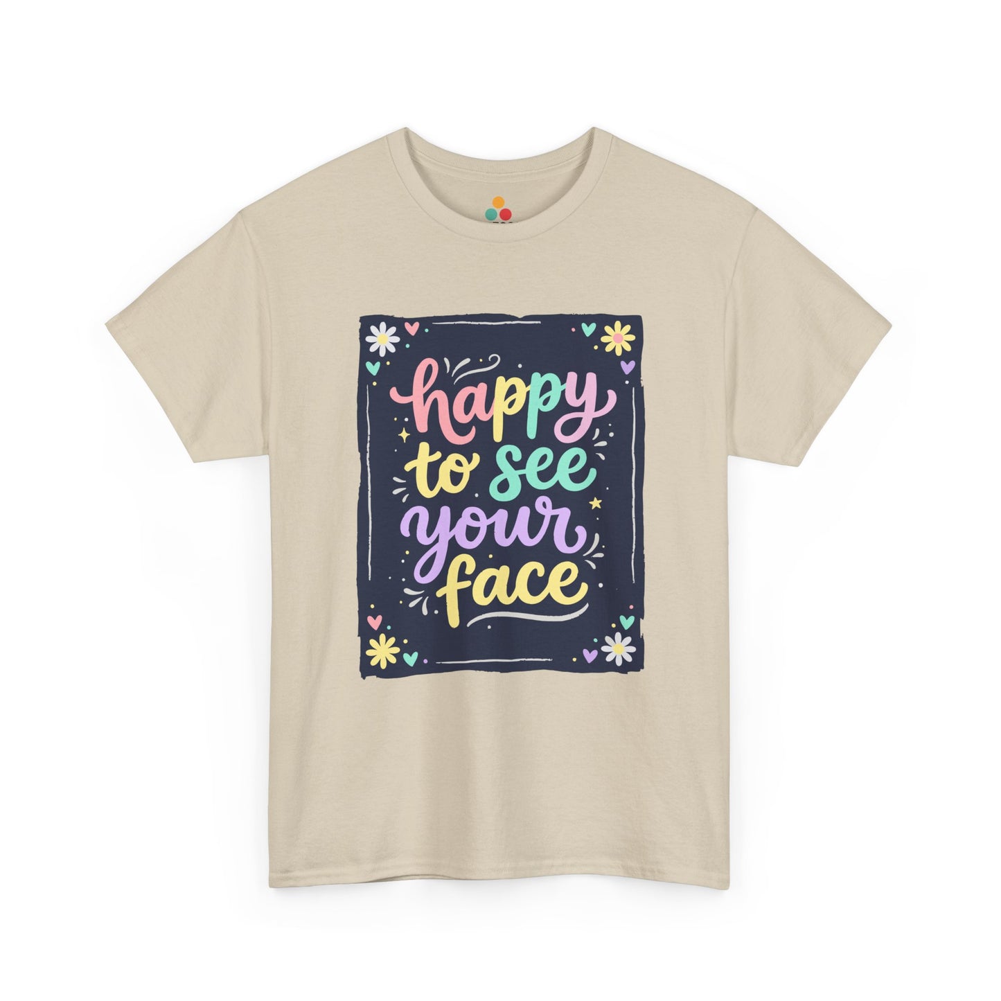 Close-up of a Beige T-shirt featuring a colorful "Happy to See Your Face" hand-lettered graphic framed with flowers and hearts on a navy background panel.
