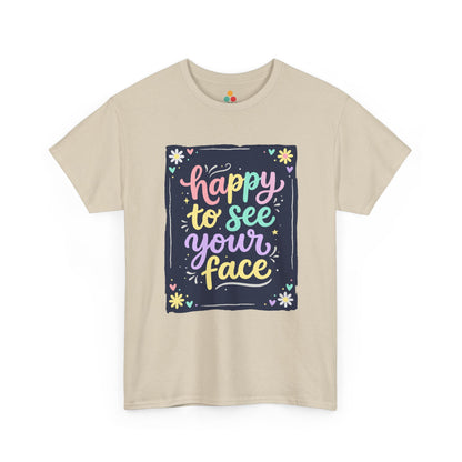 Close-up of a Beige T-shirt featuring a colorful "Happy to See Your Face" hand-lettered graphic framed with flowers and hearts on a navy background panel.
