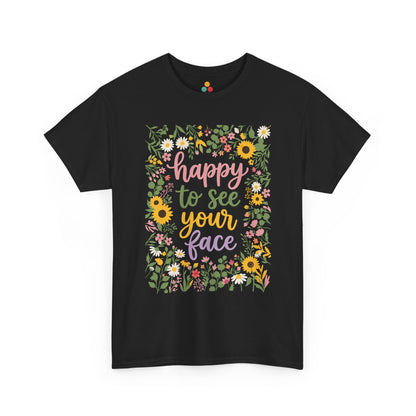 Close-up of a Black T-shirt featuring the phrase “Happy to See Your Face” in pastel lettering framed by a floral border with sunflowers and wildflowers.

