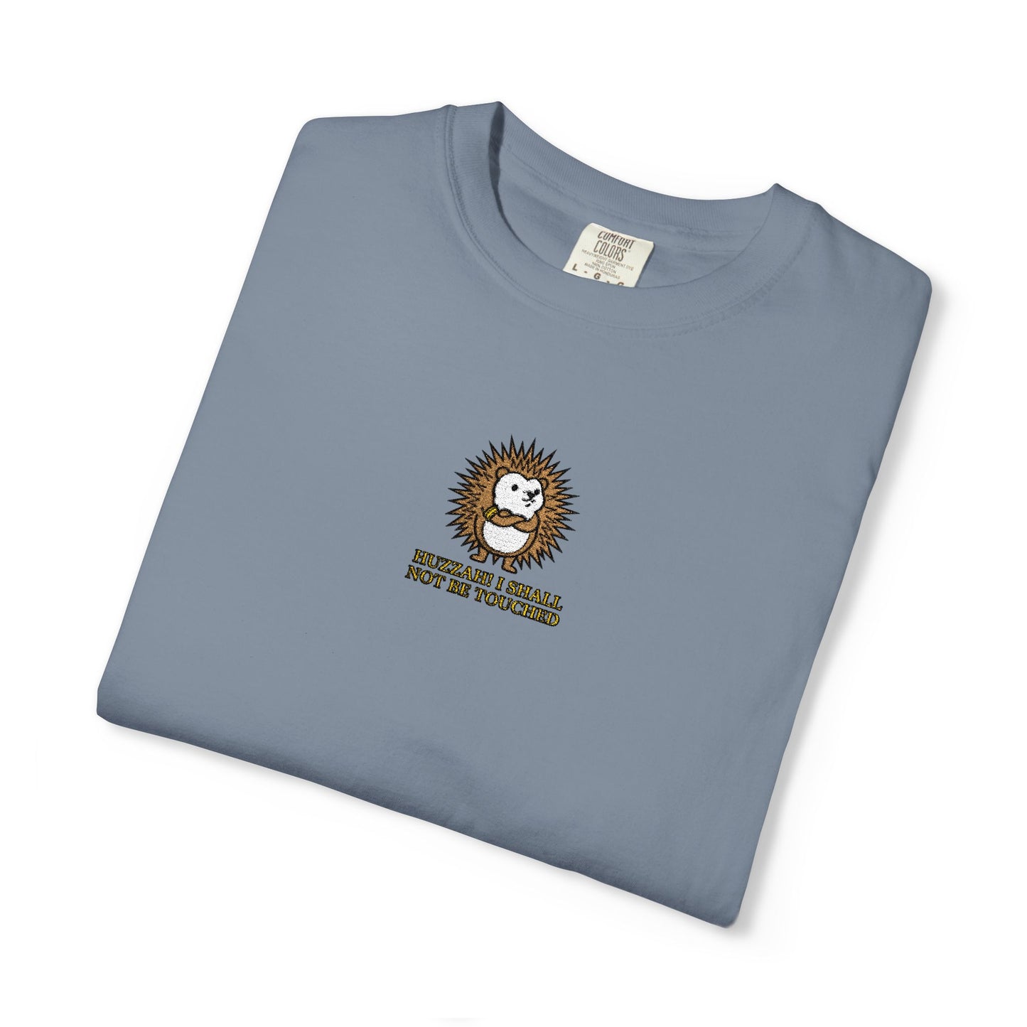Close-up of a Blue Jean Comfort Colors® shirt featuring an embroidered hedgehog with the funny saying "Huzzah! I Shall Not Be Touched."

