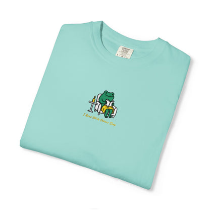  Close-up of a Chalky Mint Comfort Colors® shirt featuring a cozy green frog reading in an armchair by candlelight with the saying “I Read While Others Sleep.