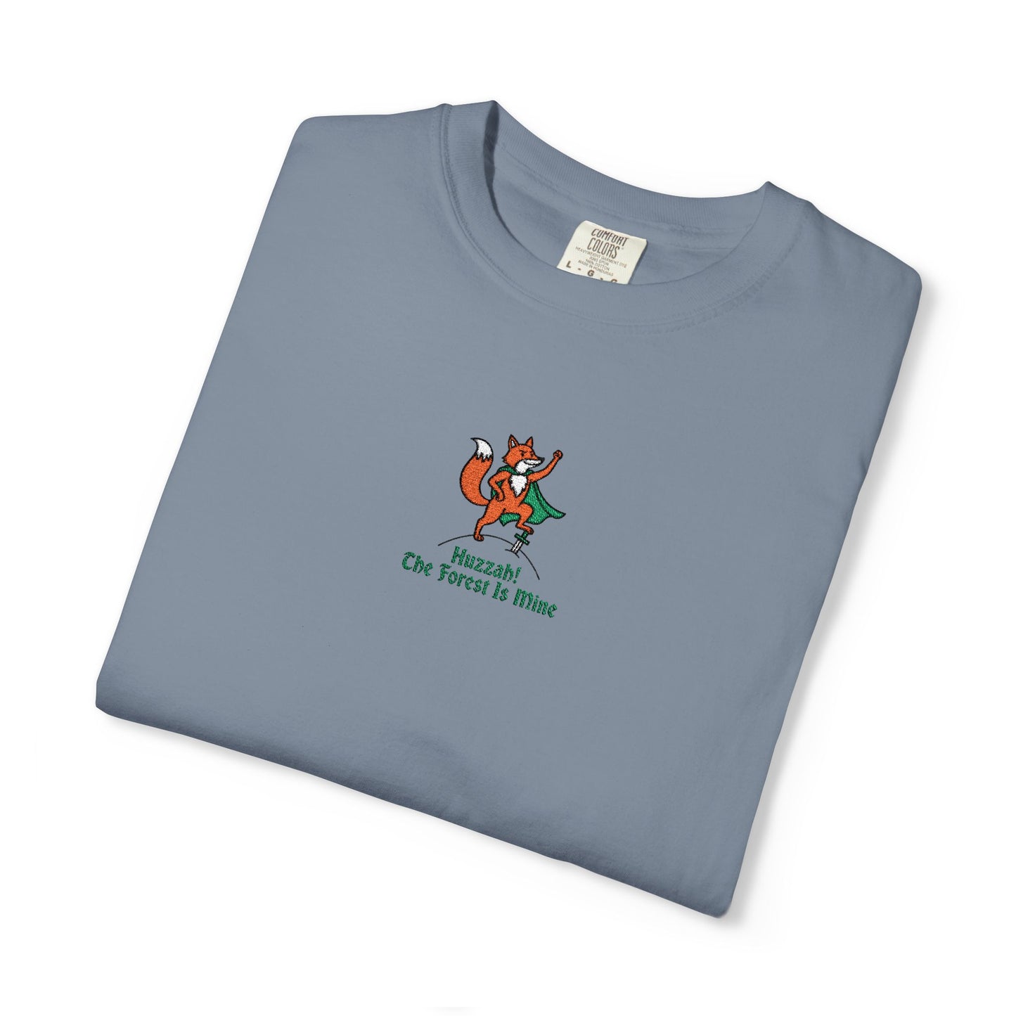 Close-up of a Comfort Colors®  Blue Jean  shirt featuring an embroidered orange fox in a green cape with the saying "Huzzah! The Forest Is Mine."

