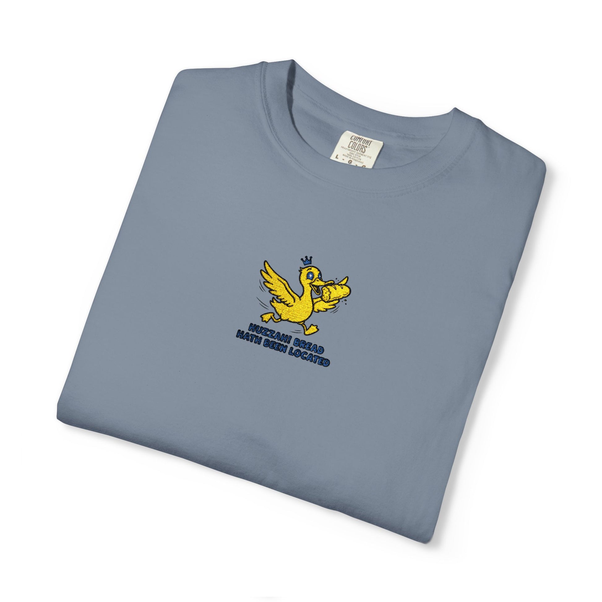 Close-up of a Comfort Colors®  Blue jean shirt featuring an embroidered yellow duck carrying bread with the saying “Huzzah! Bread Must Be Located.”


