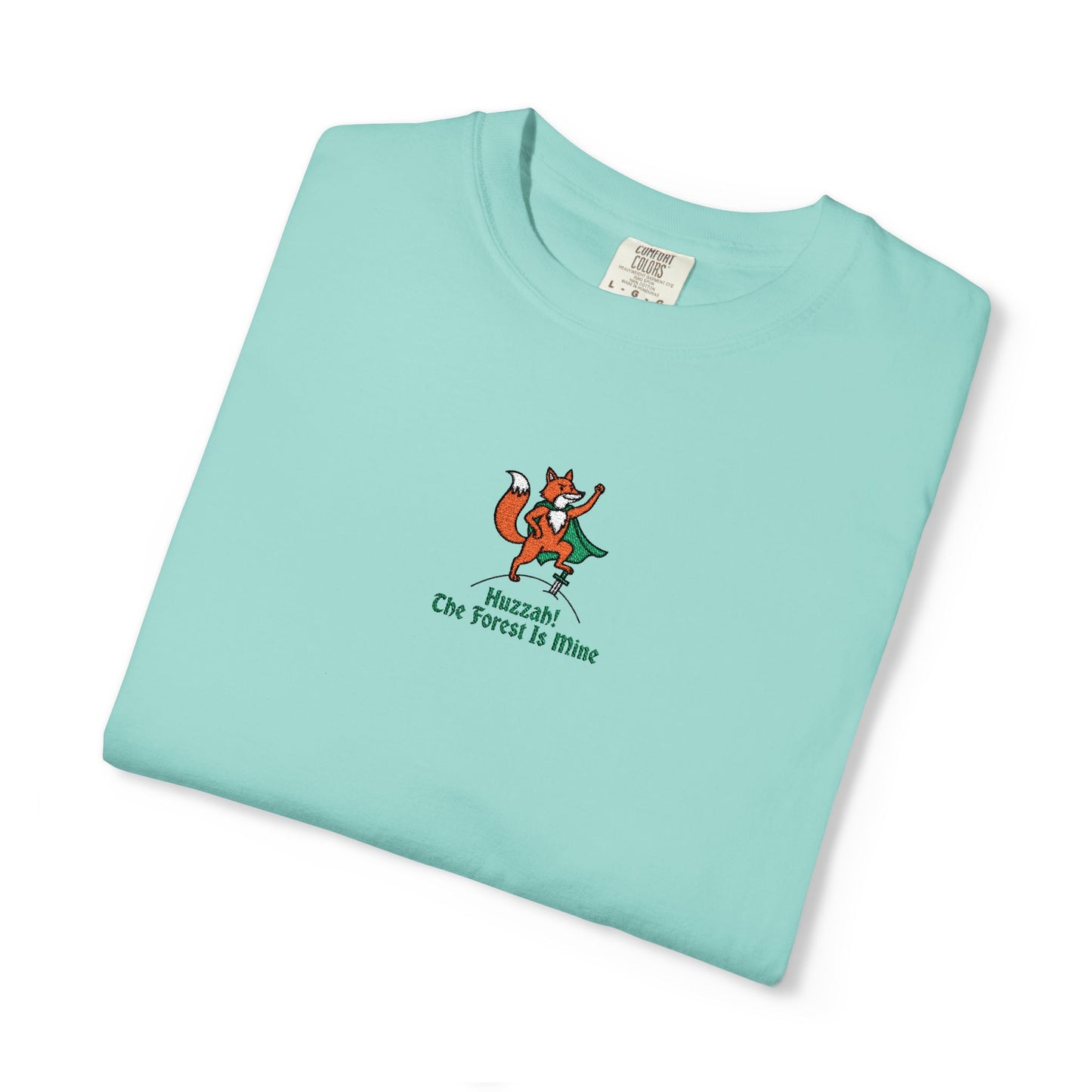 Close-up of a Comfort Colors® Chalky Mint shirt featuring an embroidered orange fox in a green cape with the saying "Huzzah! The Forest Is Mine."


