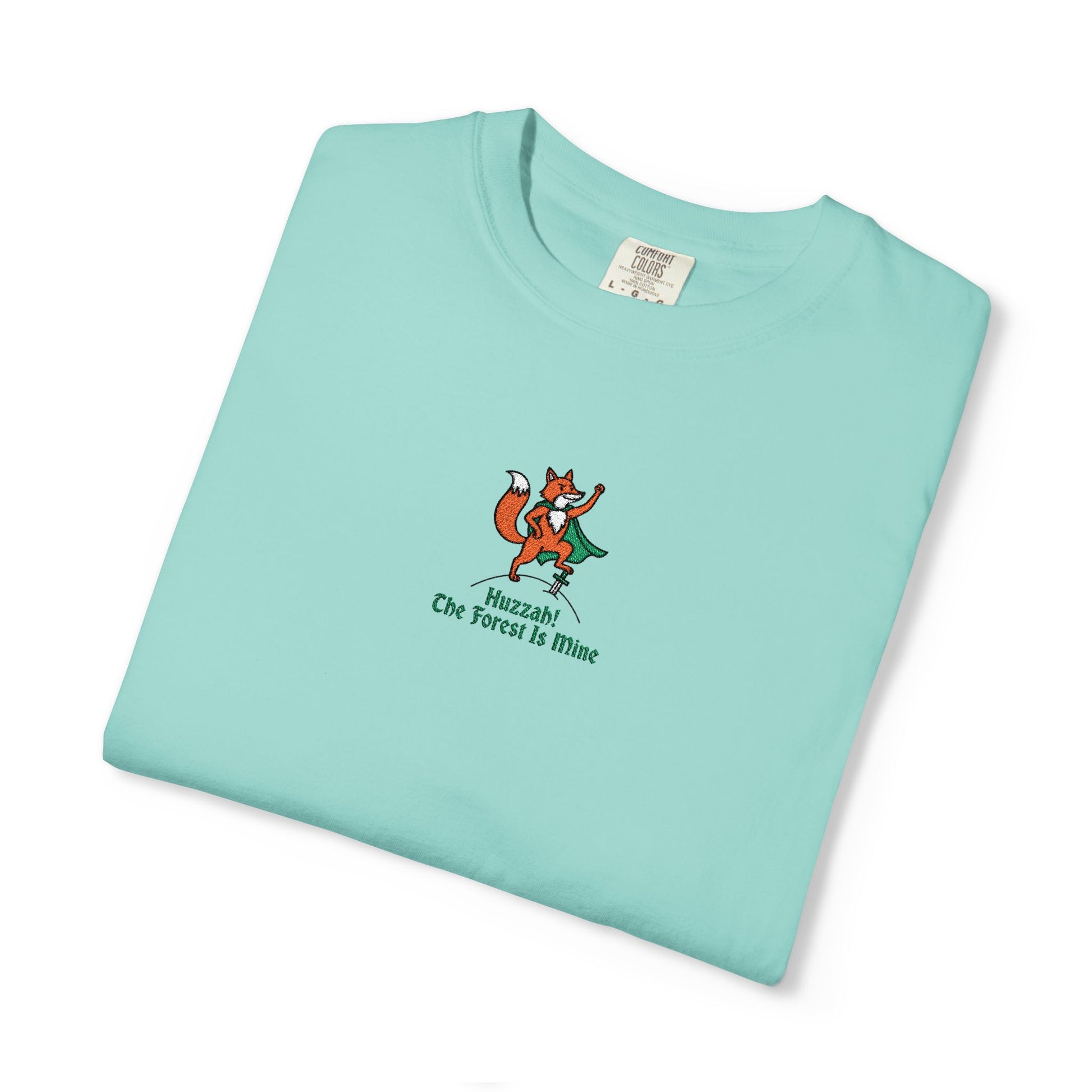 Close-up of a Comfort Colors® Chalky Mint shirt featuring an embroidered orange fox in a green cape with the saying "Huzzah! The Forest Is Mine."

