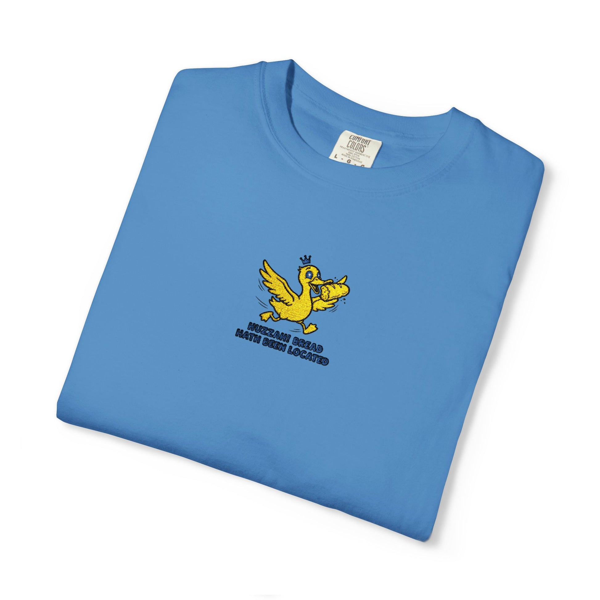 Close-up of a Comfort Colors®  Royal caribe shirt featuring an embroidered yellow duck carrying bread with the saying “Huzzah! Bread Must Be Located.”

