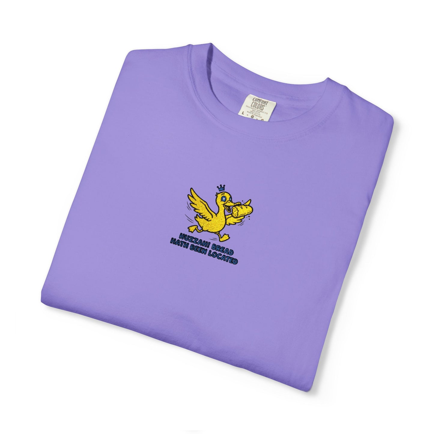 Close-up of a Comfort Colors®   Violet shirt featuring an embroidered yellow duck carrying bread with the saying “Huzzah! Bread Must Be Located.”

