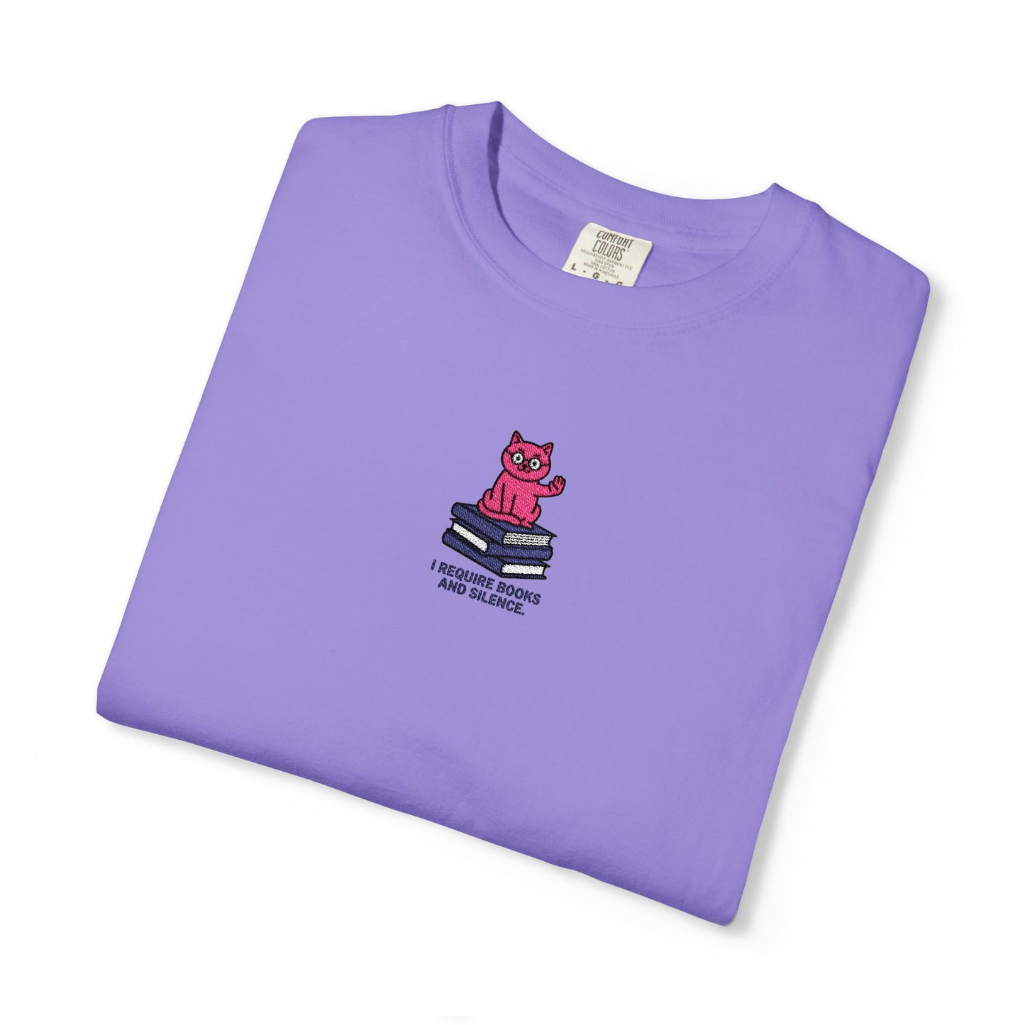   Close-up of a Comfort Colors®  Voilet shirt featuring an embroidered pink cat sitting on books with the saying “I Require Books and Silence.”

