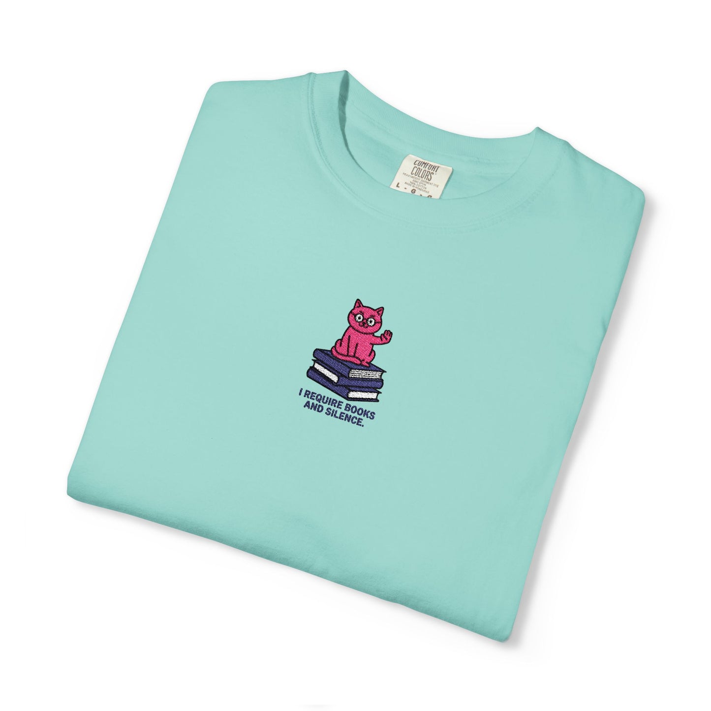  Close-up of a Comfort Colors®  chalky mint  shirt featuring an embroidered pink cat sitting on books with the saying “I Require Books and Silence.”

