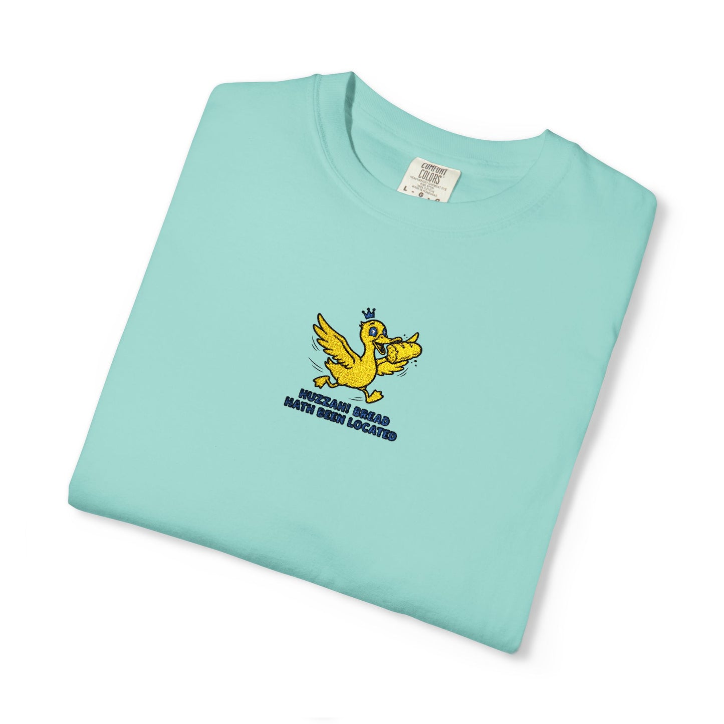 Close-up of a Comfort Colors® chalky mint shirt featuring an embroidered yellow duck carrying bread with the saying “Huzzah! Bread Must Be Located.”


