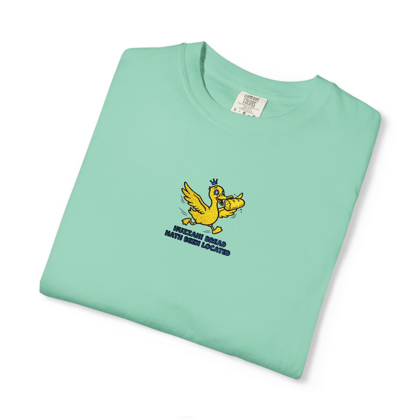 Close-up of a Comfort Colors® island reef shirt featuring an embroidered yellow duck carrying bread with the saying “Huzzah! Bread Must Be Located.”

