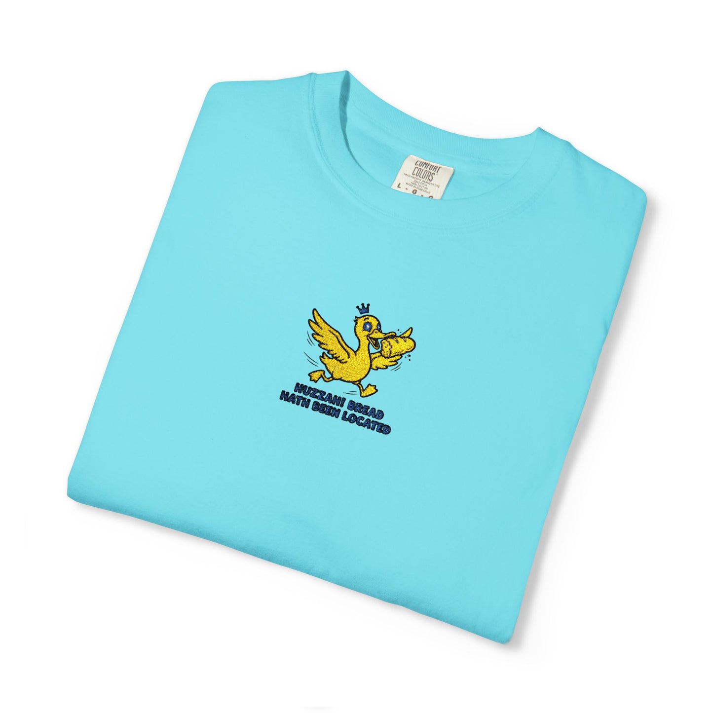 Close-up of a Comfort Colors® lagoon Blue shirt featuring an embroidered yellow duck carrying bread with the saying “Huzzah! Bread Must Be Located.”

